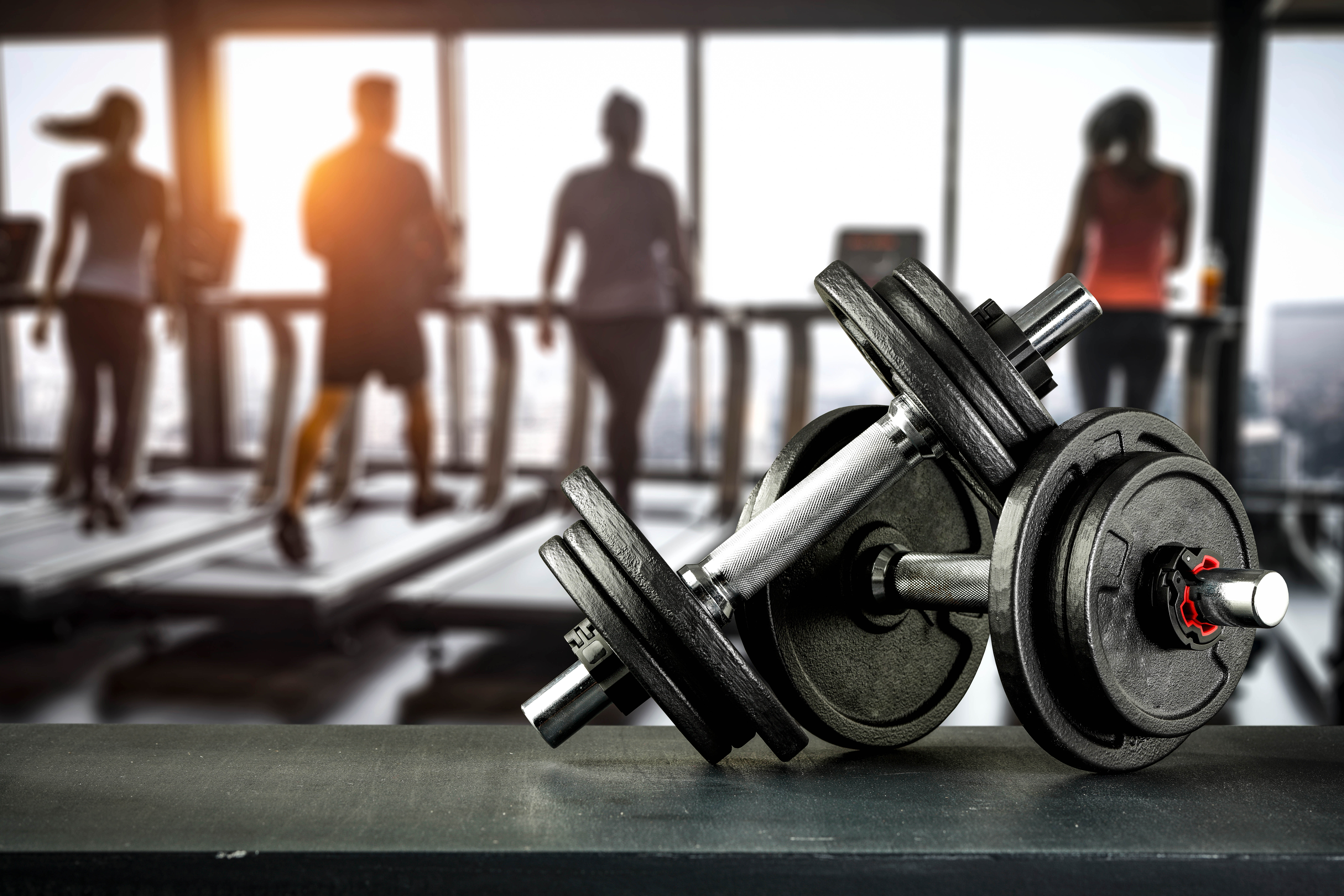 Close-up of free weights and dumbbells with gym goers blurred out in the background on the treadmills